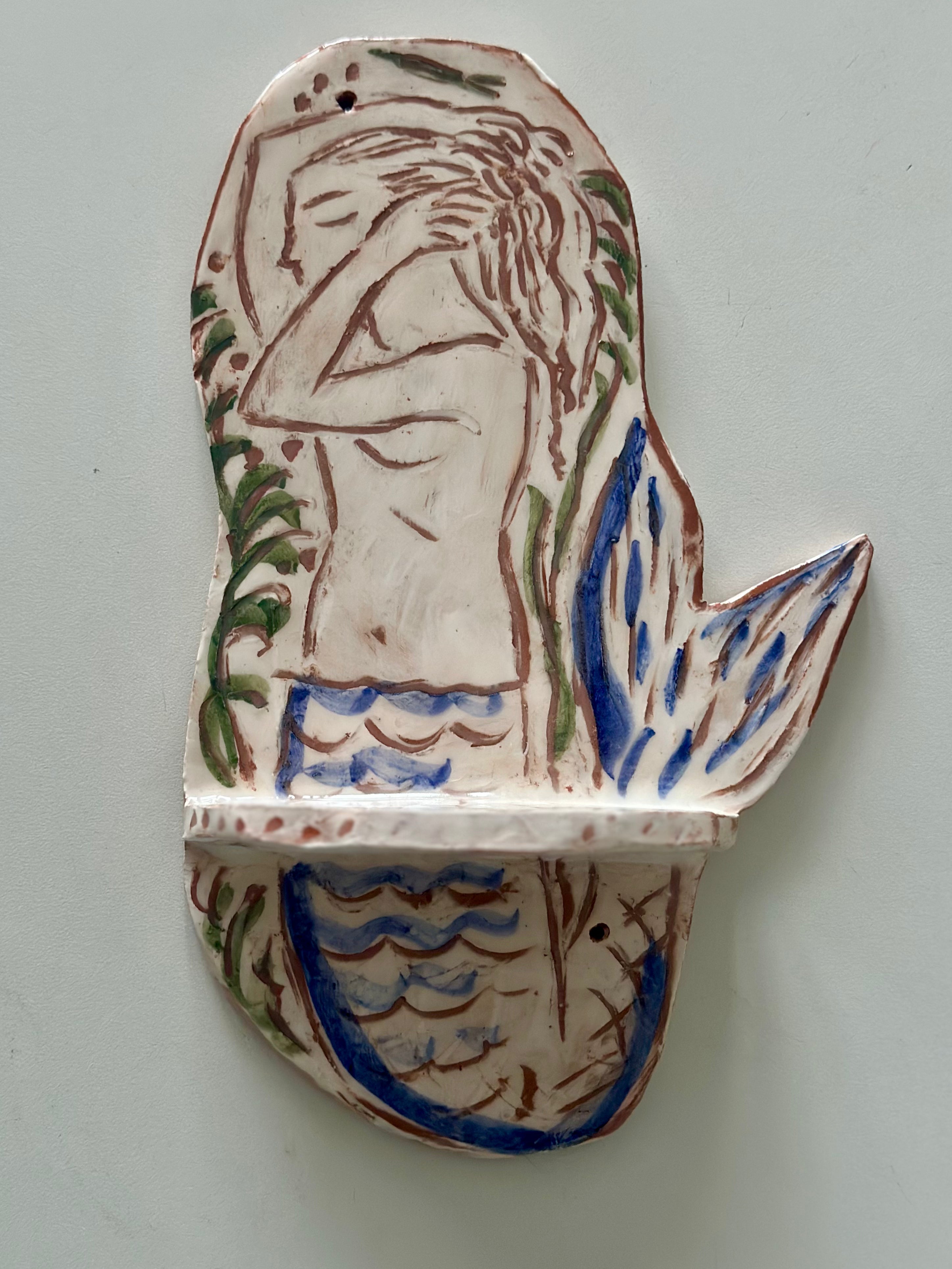 Ceramic wall art with mermaid design on a plain background