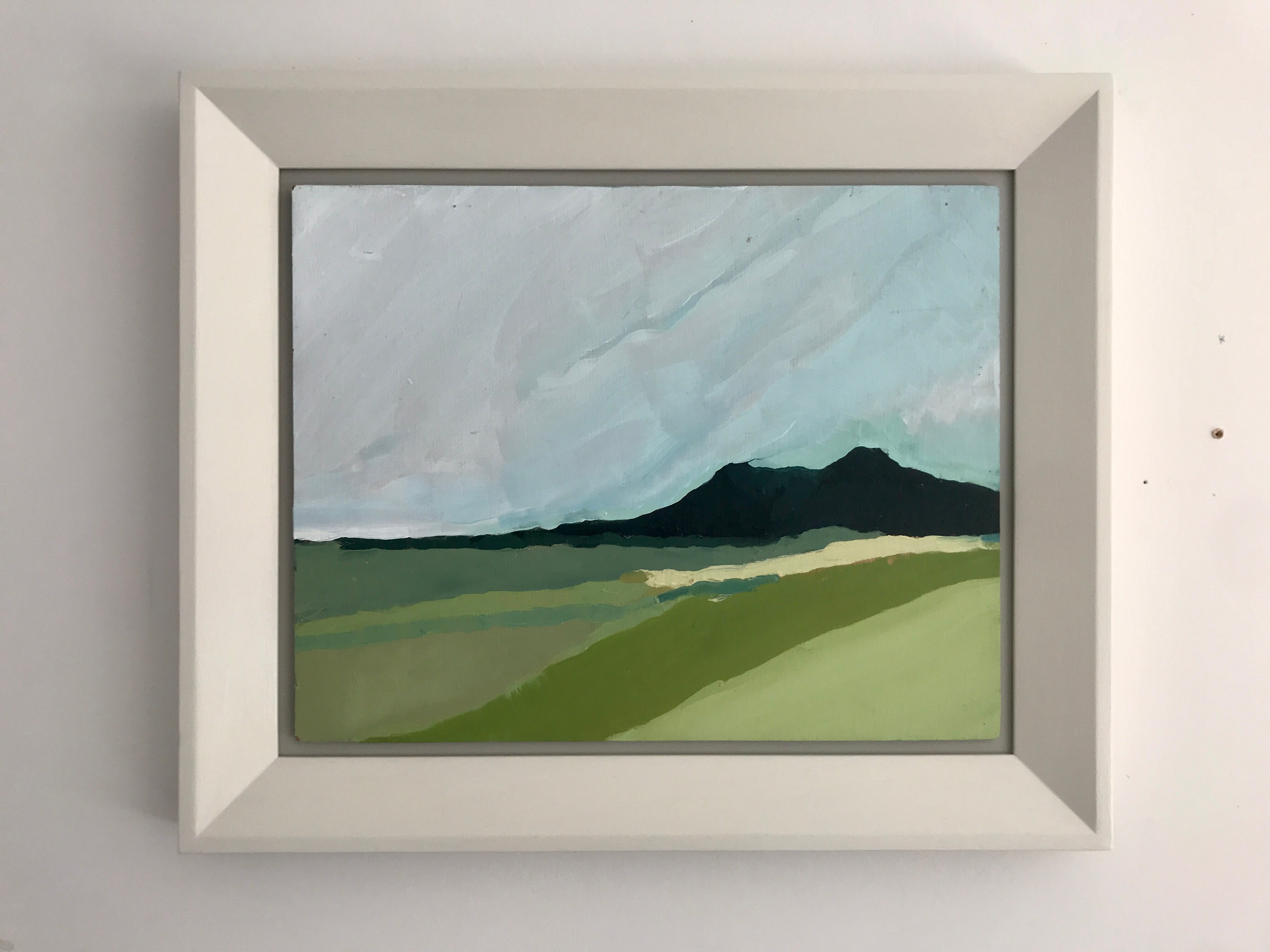 Straw by Sally Newton. Framed painting of a landscape with green fields and mountains on a grey wall.