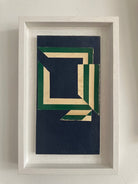 A framed paper collage artwork featuring geometric shapes in blue and green colors with a white border.